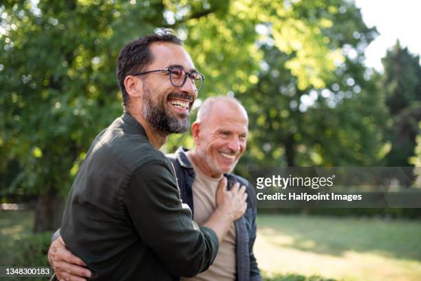 senior man with his mature son embracing outdoors in park. - hand on shoulder stock pictures, royalty-free photos & images