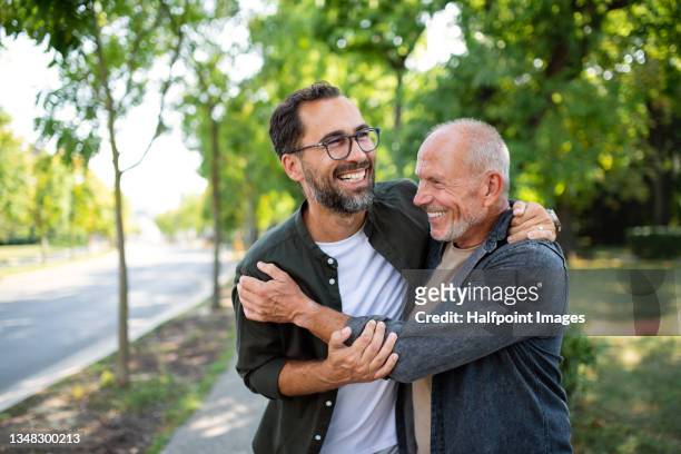 senior man with his mature son embracing outdoors in park. - senior heureux photos et images de collection