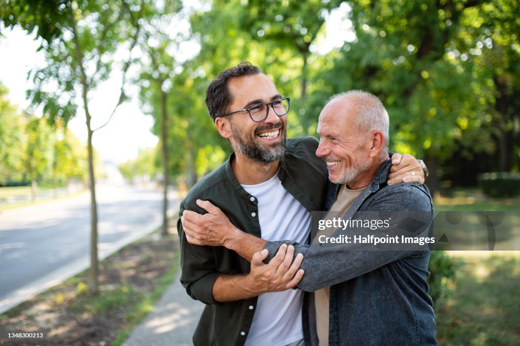 Senior man with his mature son embracing outdoors in park.