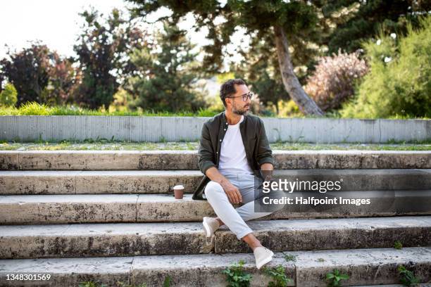 portrait of happy mature man with smartphone resting outdoors in park, looking away. - leisure work coffee happy stockfoto's en -beelden