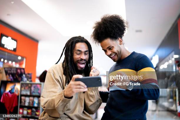 hermanos viendo deportes o jugando en el teléfono inteligente en el centro comercial - brazilian playing football fotografías e imágenes de stock