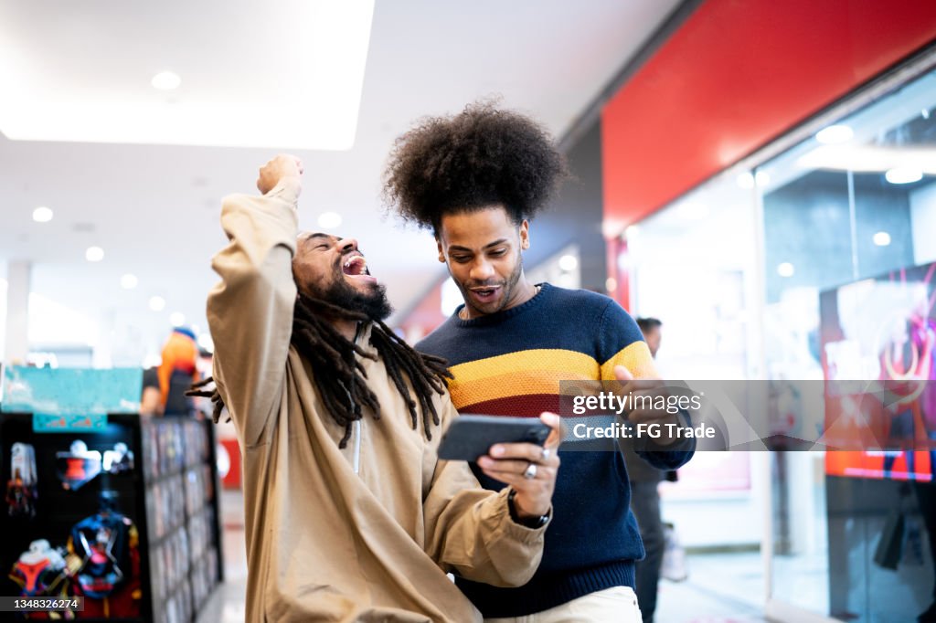 Hermanos viendo deportes o jugando en el teléfono inteligente en el centro comercial