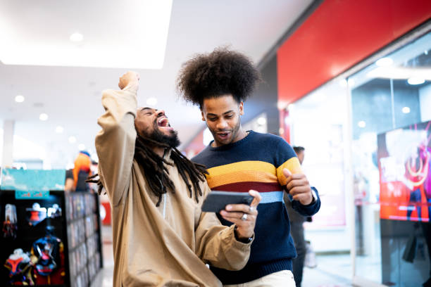 brothers watching sports or playing on the smartphone at the mall - black person using phone celebrating stock pictures, royalty-free photos & images
