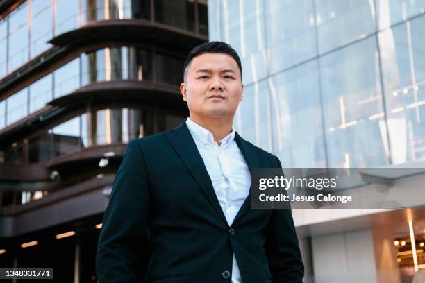 portrait of a chinese man with suit's jacket. looking at the camera, with cold and serious expression. with a background of office buildings. job, future, economy and chinese concept - businessman in suit ストックフォトと画像