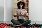 Multiracial young woman meditating with hands in prayer at home