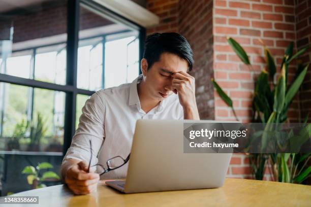 stressed and tired young businessman working with laptop - man rubbing eyes stock pictures, royalty-free photos & images