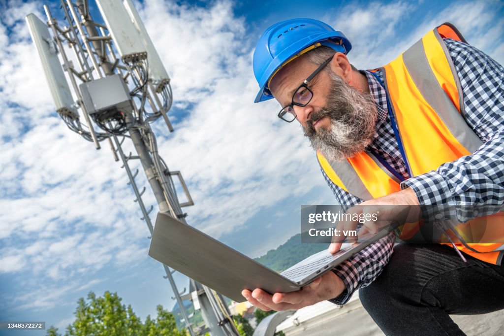Bearded technician in reflective vest working on laptop computer outdoors