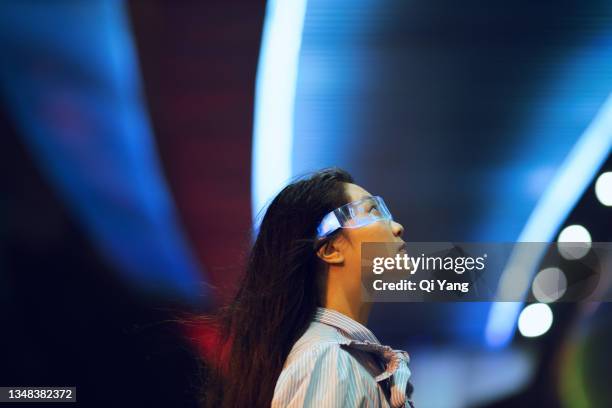 young asian woman standing under the illuminated pedestrian bridge at night looking into the distance - bridge stock photos et images de collection