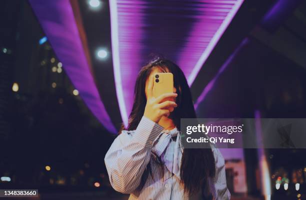 young asian woman using mobile phone while standing under a pedestrian bridge glowing at night - 隠れる ストックフォトと画像