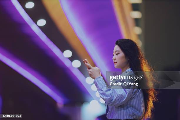 young asian woman using mobile phone while standing under a pedestrian bridge glowing at night - angeleuchtet zahlen mensch stock-fotos und bilder