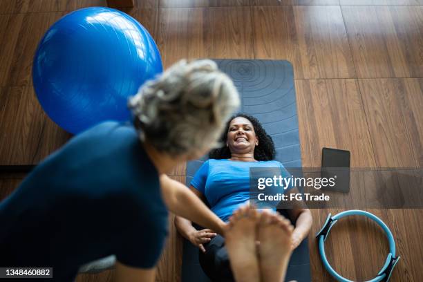 instruktor hilft einer reifen frau beim training in einem pilates-studio - sportmedizin happy stock-fotos und bilder