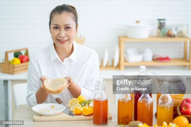 asian senior woman hold scoby that use for making kombucha drink and can be mixed with various types of fruit - kombucha stockfoto's en -beelden