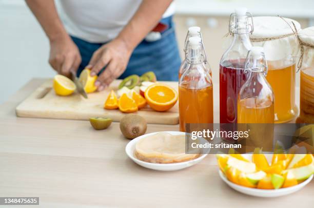 hands of man prepare kombucha drink from various types of component and ingredient with different types of fruits in kitchen - kombucha stockfoto's en -beelden