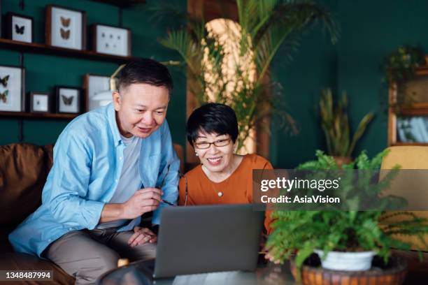 cheerful senior asian couple using laptop together while relaxing at home. elderly and technology - senior financial planning stock pictures, royalty-free photos & images