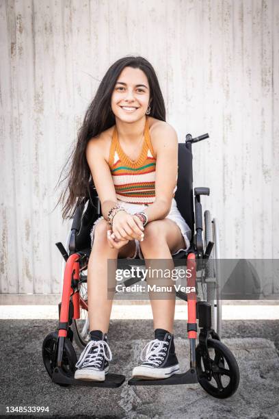 long-haired young woman with a disability sitting in a wheelchair smiling in spite of adversity. - junge frau im rollstuhl stock-fotos und bilder