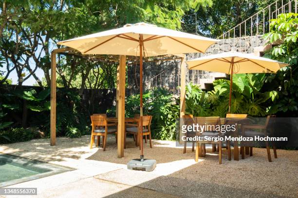 chairs under parasol umbrellas in front of the swimming pool in a beautiful boutique spa hotel resort in tepoztlan, mexico - gartenschirm stock-fotos und bilder
