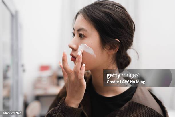 an asian girl is using cosmetics in front of a mirror - crema solare foto e immagini stock