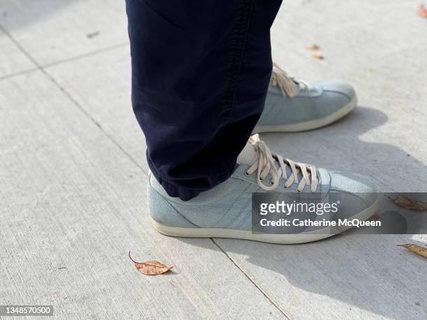partial view of man wearing light blue canvas sneakers & navy denim pants standing on sidewalk - stationery close up stock pictures, royalty-free photos & images