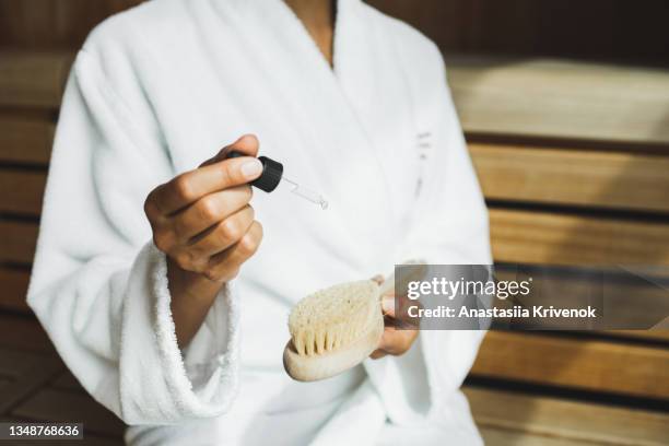 woman drips essential or moisturizing oil on massage cactus owl massage brush in sauna. - natural organic thermo cosmetics stockfoto's en -beelden