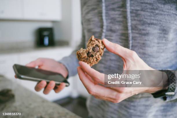 man snacks on cookie while looking at his smart phone - flapjack stock pictures, royalty-free photos & images