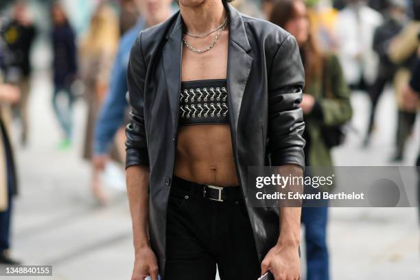 Guest wears silver chain necklaces, a black shiny leather blazer jacket, a black shiny leather with white large seams shoulder-off / cropped top, a...
