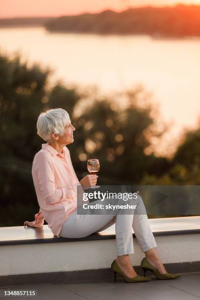 pensive senior woman enjoying in wine on a rooftop at sunset. - senior women wine stock pictures, royalty-free photos & images