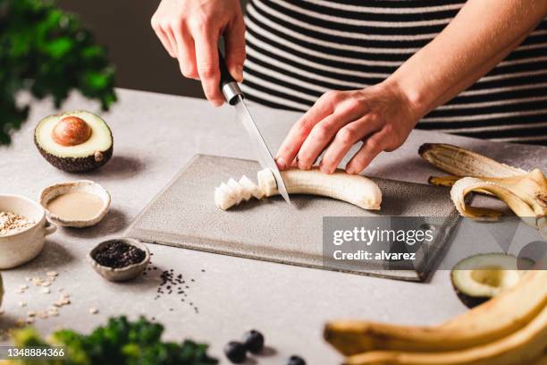 woman chopping banana for making smoothie bowl in kitchen - chopped stock pictures, royalty-free photos & images