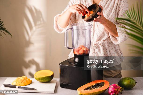 woman preparing smoothie in kitchen - mango juice stockfoto's en -beelden