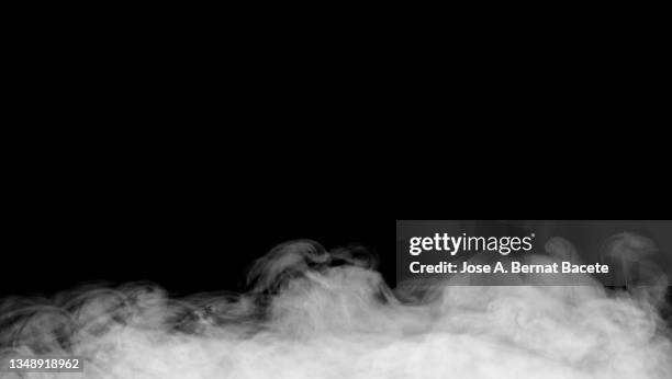 full frame of white smoke cloud floating on the ground on a black background. - smoke stockfoto's en -beelden