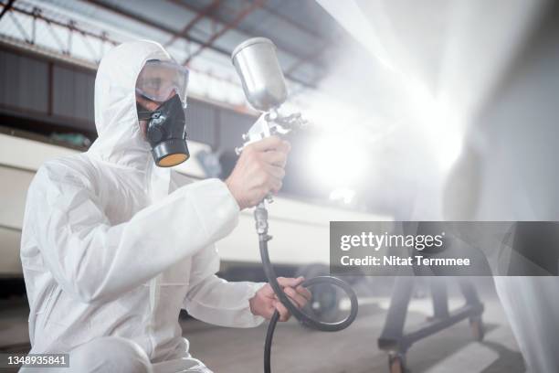 painting technician applying paint to a boat outer surface part with a airbrush gun or pressurized spray gun in a boat repair body workshop. - lack stock-fotos und bilder