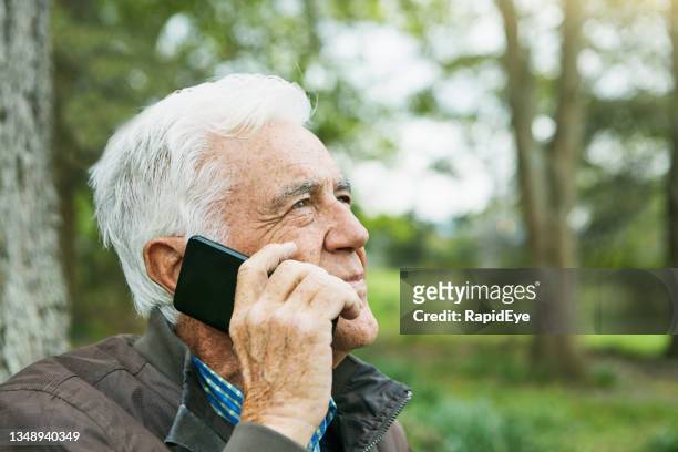 handsome man in his late 70s holding his mobile phone and listening intently - listening intently stock pictures, royalty-free photos & images