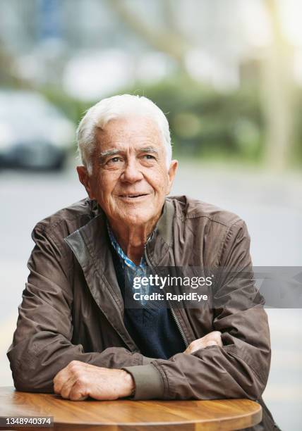 handsome man in his late 70s looks cheerful as he sits outdoors at a sidewalk cafe table - city 70's stock pictures, royalty-free photos & images