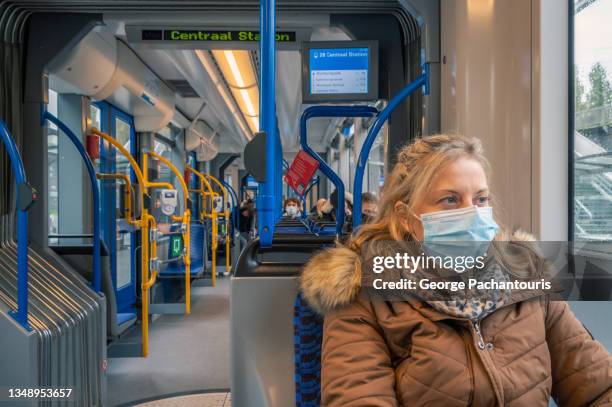 woman with facemask and warm clothes in public transportation looking outside the window - máscara-protectora fotografías e imágenes de stock