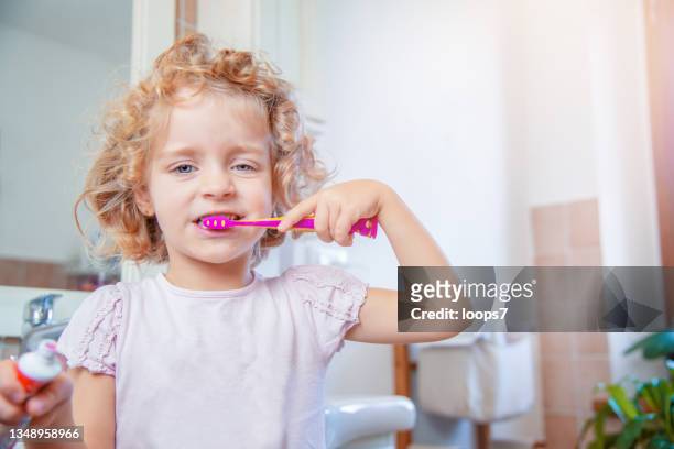cabello rubio niña de cinco años cepillándose los dientes en el baño - usar la boca fotografías e imágenes de stock