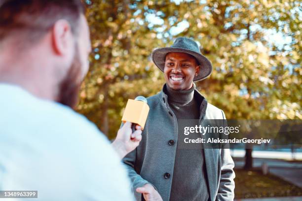 un homme africain souriant passe et donne une déclaration rapide au sondage d’un journaliste - homme micro photos et images de collection