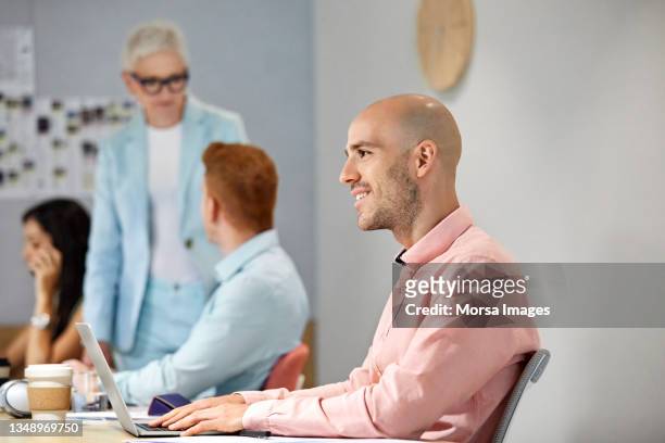 smiling executive using laptop while looking away - trefferversuch stock-fotos und bilder