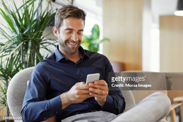 smiling businessman using smart phone at office - man smartphone stock pictures, royalty-free photos & images