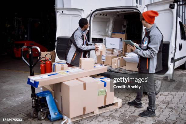 delivery man working on digital tablet while organising packages for shipment in a van with his coworker - delivery truck stock pictures, royalty-free photos & images