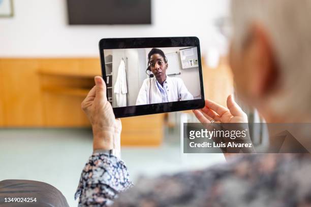 sick woman at home video conferencing with doctor using telmedicine digital tablet - remote location stock pictures, royalty-free photos & images