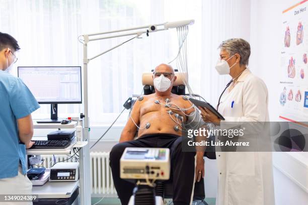 cardiologist with senior patient on ecg bicycle during therapy session in clinic - womans clinic heart stockfoto's en -beelden