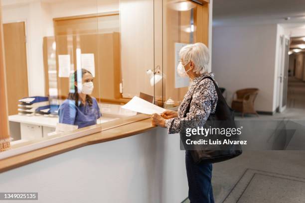 nurse assisting a senior patient at the hospital reception desk - visit stock-fotos und bilder