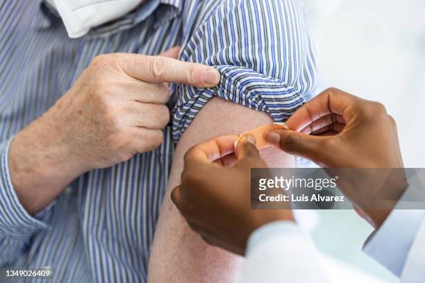 close-up of a doctor putting a band-aid on the arm of a male after giving vaccine - applying plaster stock pictures, royalty-free photos & images