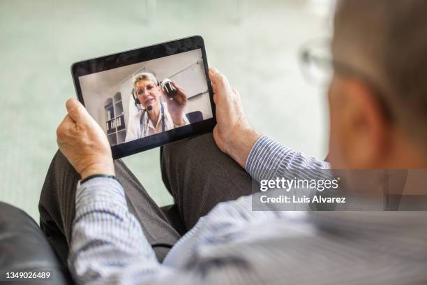 senior man having telemedicine online consultation with female doctor at home on digital tablet - tablet screen stock-fotos und bilder