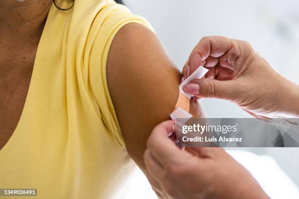 female doctor hands putting band-aid on woman arm after giving vaccine - influenza vaccination stock pictures, royalty-free photos & images