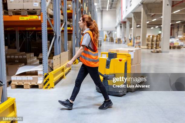 woman dispatcher pulling boxes on pallet truck at the warehouse - female factory stockfoto's en -beelden