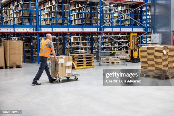 employee walking with packages on a trolley at distribution warehouse - pallet jack stock pictures, royalty-free photos & images