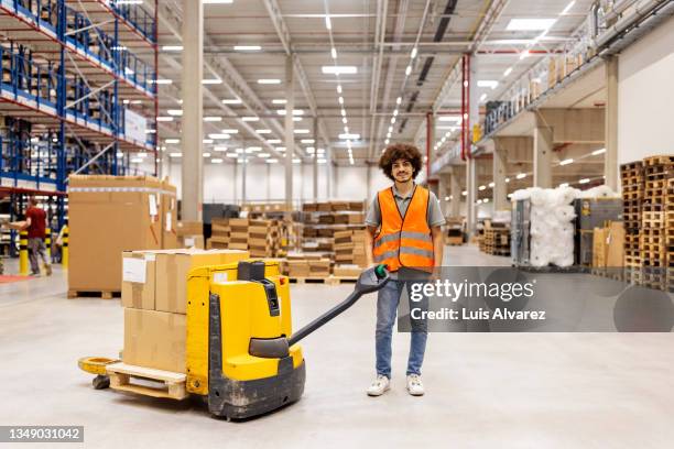 portrait of a young man with hand pallet jack standing in warehouse - pallet jack stock pictures, royalty-free photos & images