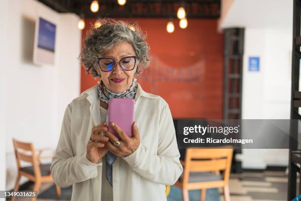 une femme latine de 50 ans est au bureau en travaillant avec son téléphone portable - 50 year old photos et images de collection