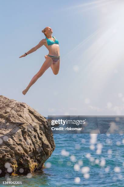 artistic flight of teenage girl jumping off a cliff during summer vacation at the sea - young teen girl beach foto e immagini stock