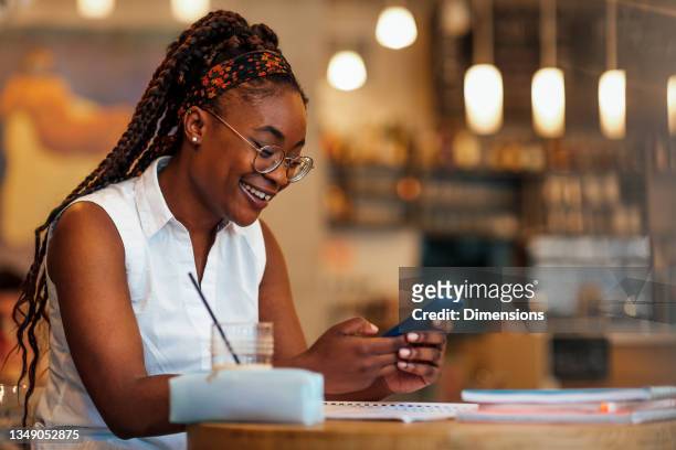 mujer negra usando el teléfono celular en el café - mobile learning fotografías e imágenes de stock